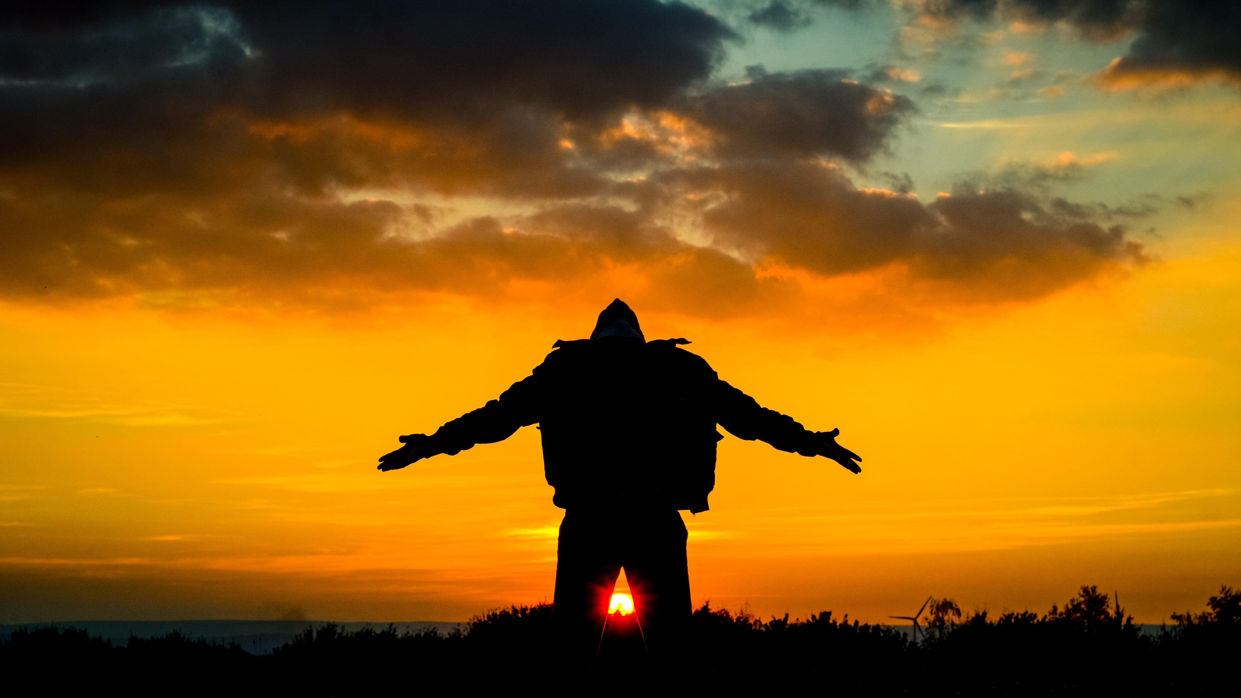 A person  holding their arms out to their sides and up with their hands palm up and their head back looking to the orange setting sun sky.